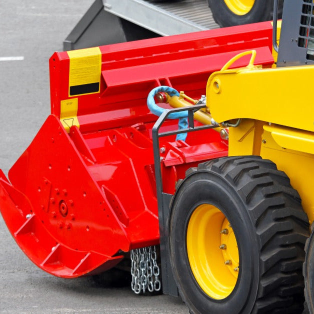 A close-up of a yellow skid steer with a bright red attachment parked on a section of concrete with painted lines.