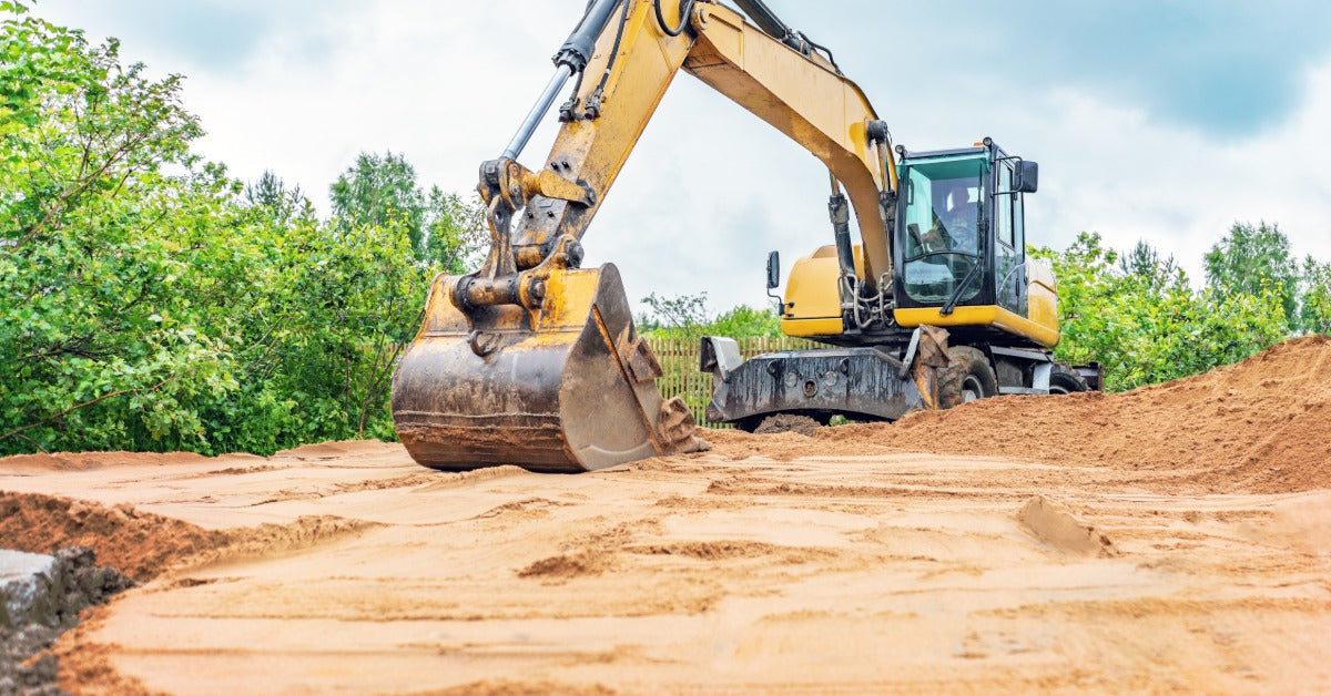 An operator in a yellow excavator using a bucket attachment to smooth a sandy surface on the jobsite.