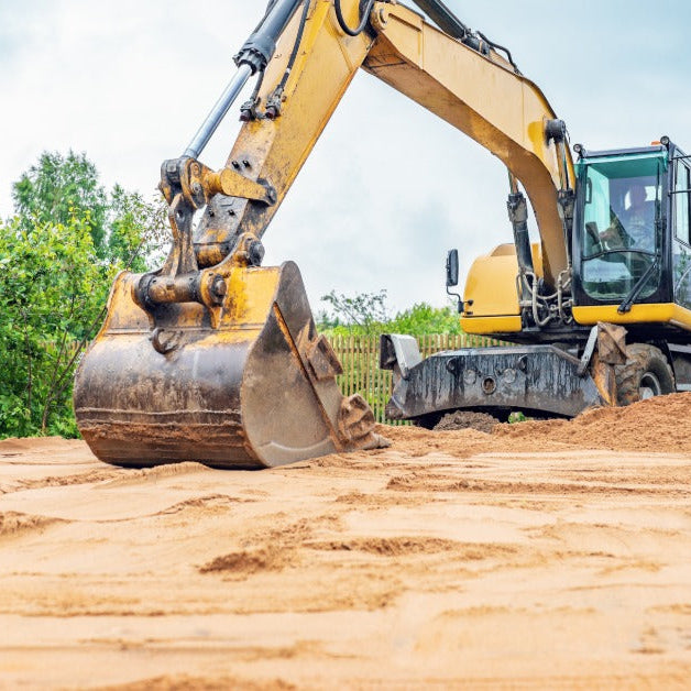 An operator in a yellow excavator using a bucket attachment to smooth a sandy surface on the jobsite.
