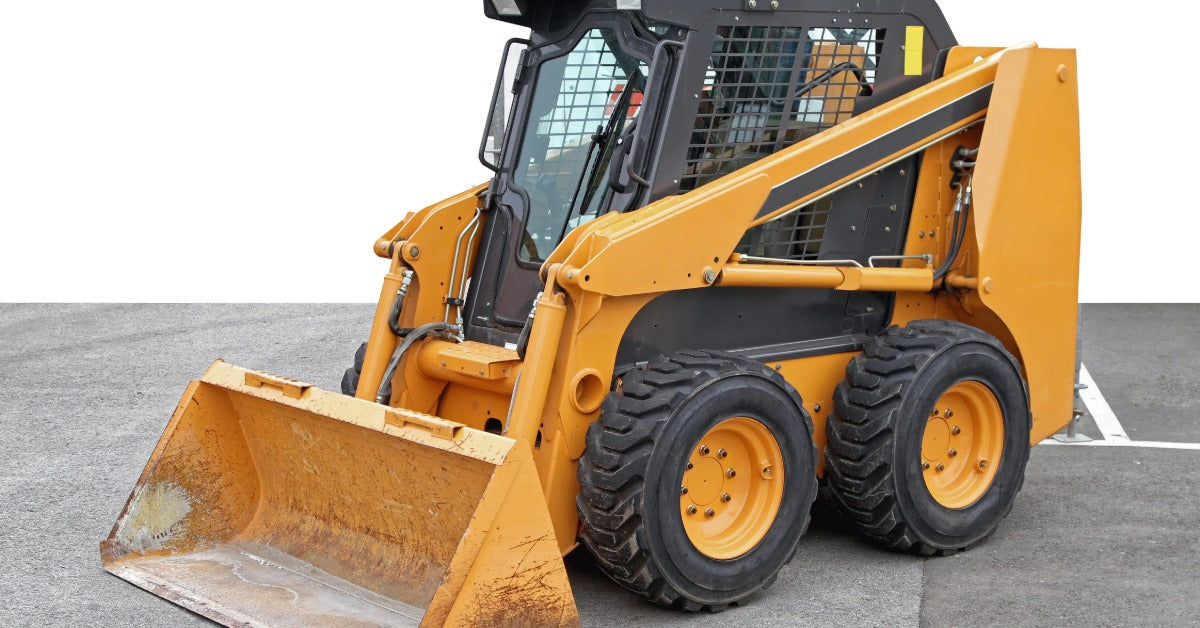 A yellow skid steer with a yellow bucket attachment parked on a paved surface next to a large white building.