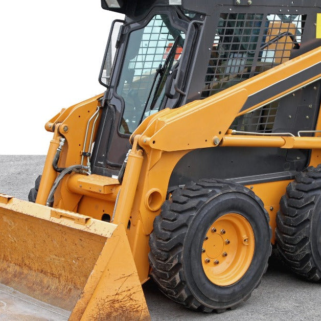 A yellow skid steer with a yellow bucket attachment parked on a paved surface next to a large white building.