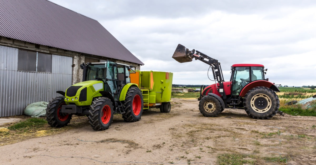 Two tractors operating on a farm. One tractor has a bucket attachment and the other is pulling a trailer with a feed distributor.